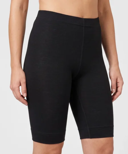 Kvinlig modell visar ett par svarta korta lager-1 underställsbyxor i 100% merinoull. Modellen visar byxorna framifrån i en studio med ljusgrå bakgrund.