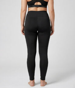 Kvinnlig modell visar ett par svarta enklare träningstights med hög midja. Modellen strår framifrån i en studio med ljusgrå bakgrund.