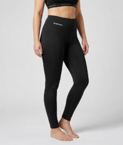 Kvinnlig modell visar ett par svarta enklare träningstights med hög midja. Modellen strår framifrån i en studio med ljusgrå bakgrund.