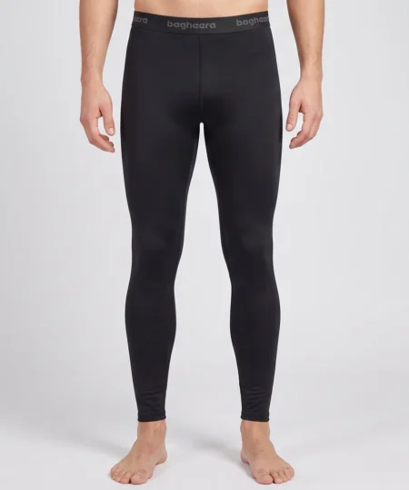 Manlig modell visar ett par svarta Clima Pants lager-2 underställsbyxor. Modellen visar byxorna framifrån i en studio med ljusgrå bakgrund.
