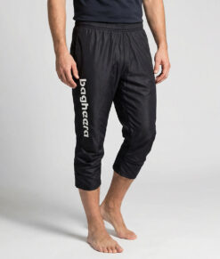 Manlig modell visar ett par svarta knälånga tunna orienteringsbyxor. Modellen strår snett framifrån i en studio med ljusgrå bakgrund.