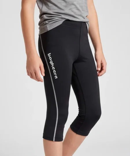 Pojkmodell visar ett par svarta knätights. Modellen visar tightsen snett framifrån i en studio med ljusgrå bakgrund.