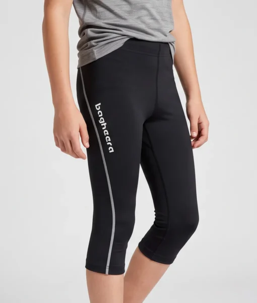 Pojkmodell visar ett par svarta knätights. Modellen visar tightsen snett framifrån i en studio med ljusgrå bakgrund.