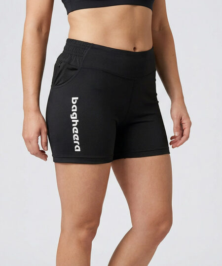 Kvinnlig modell visar ett par svarta korta träningstights. Modellen står snett framifrån i en studio med ljusgrå bakgrund.