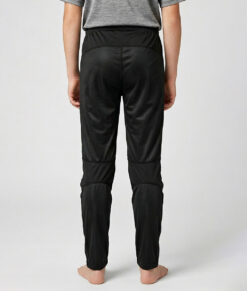 Killmodell i 12 års åldern visar ett par svarta långa tunna orienteringsbyxor. Modellen strår bakifrån i en studio med ljusgrå bakgrund.