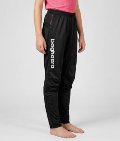 Tjejmodell i 12 års åldern visar ett par svarta långa tunna orienteringsbyxor. Modellen strår snett framifrån i en studio med ljusgrå bakgrund.