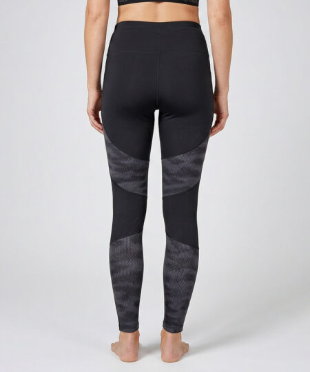 Kvinnlig modell visar ett par svarta mörkgrå träningstights med hög midja och mönstrad mesh. Modellen strår bakifrån i en studio med ljusgrå bakgrund.