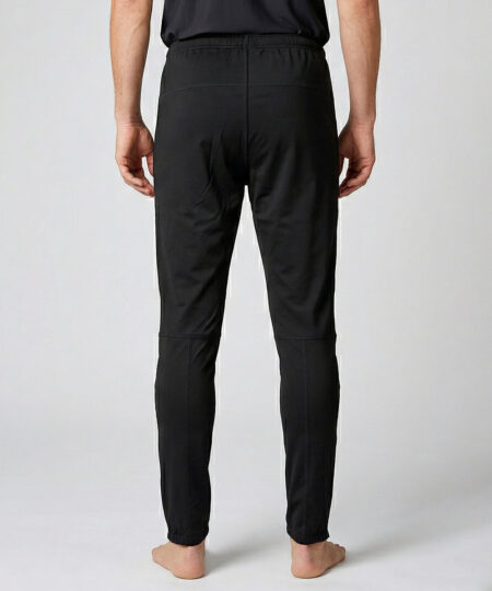 Manlig modell visar ett par svarta långa funktionsträningsbyxor. Modellen står bakifrån i en studio med ljusgrå bakgrund.