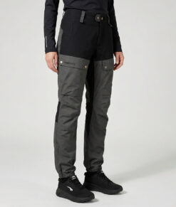 Kvinlig modell visar ett par gråa långa friluftsbyxor. Modellen står snett framifrån i en studio med ljusgrå bakgrund.