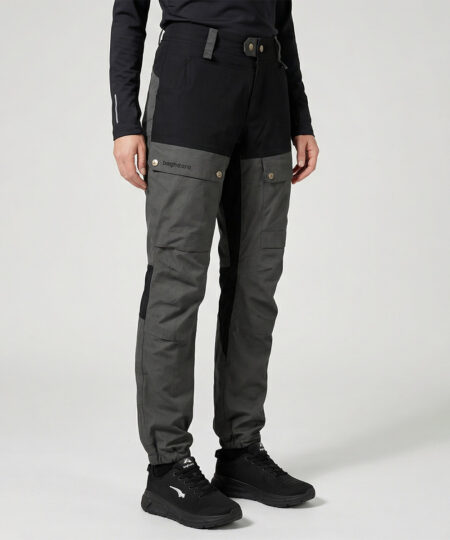 Kvinlig modell visar ett par gråa långa friluftsbyxor. Modellen står snett framifrån i en studio med ljusgrå bakgrund.