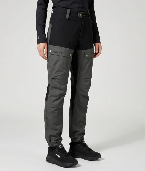 Kvinlig modell visar ett par gråa långa friluftsbyxor. Modellen står snett framifrån i en studio med ljusgrå bakgrund.