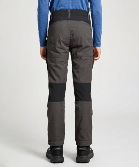 Pojkmodell ca 12 år visar ett par gråa långa friluftsbyxor. Modellen står snett bakifrån i en studio med ljusgrå bakgrund.