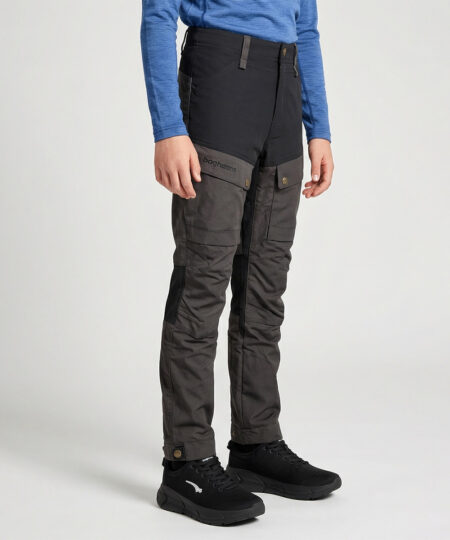 Pojkmodell ca 12 år visar ett par gråa långa friluftsbyxor. Modellen står snett framifrån i en studio med ljusgrå bakgrund.