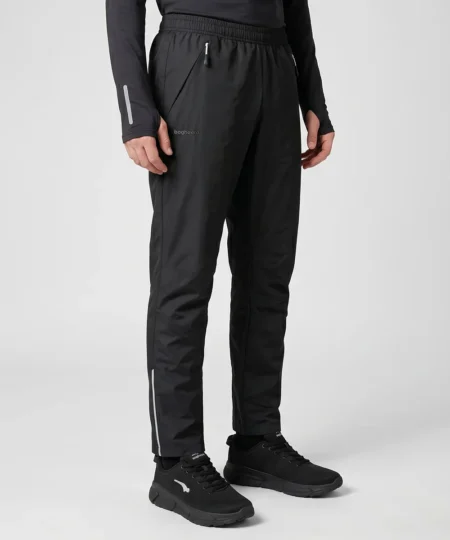 Manlig modell visar ett par svarta skalbyxor. Modellen visar byxorna snett framifrån i en studio med ljusgrå bakgrund.