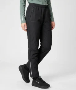 Kvinlig modell visar ett par svarta skalbyxor. Modellen visar byxorna snett framifrån i en studio med ljusgrå bakgrund.