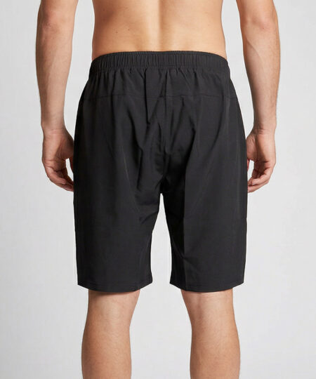 Manlig modell visar ett par svarta längre shorts. Modellen står bakifrån i en studio med ljusgrå bakgrund.