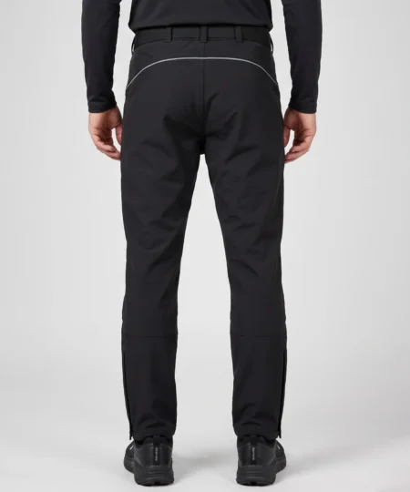 Manlig modell visar ett par svarta vinter softshell byxor. Modellen står bakifrån i en studio med ljusgrå bakgrund.