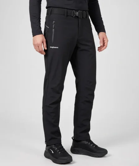 Manligmodell visar ett par svarta vinter softshell byxor. Modellen står snett framifrån i en studio med ljusgrå bakgrund.