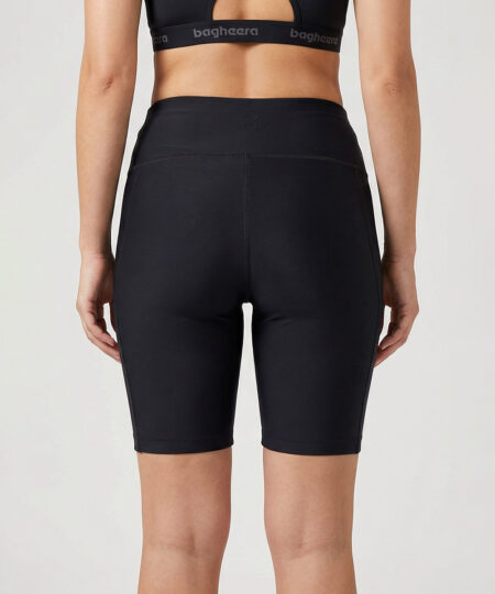 Kvinnlig modell visar ett par svarta korta tights i funktionsmaterial. Modellen har handen i fickan för att visa att det finns fickor på benen. Modellen står bakifrån i en studio med ljusgrå bakgrund.