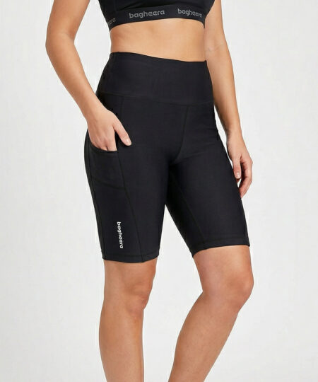 Kvinnlig modell visar ett par svarta korta tights i funktionsmaterial. Modellen har handen i fickan för att visa att det finns fickor på benen. Modellen står framifrån i en studio med ljusgrå bakgrund.