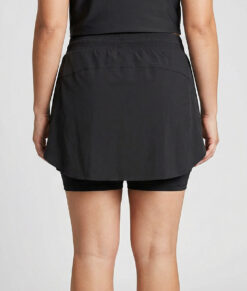 Kvinnlig modell visar en svart skort, kjol med innertights. Modellen står bakifrån i en studio med ljusgrå bakgrund.