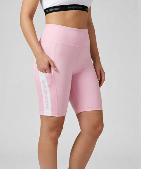 Kvinlig modell visar ett par rosa korta tights. Modellen har ena handen i fickan för att visa att tightsen har fickor. Modellen står snett framifrån i en studio med ljusgrå bakgrund.