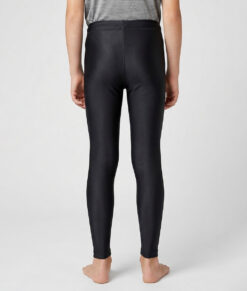 En killmodell i 12 års åldern visar ett par svarta enklare långa tights. Modellen står bakifrån i en studio med ljusgrå bakgrund.