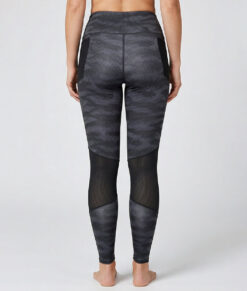 Kvinnlig modell visar ett par mörkgrå svarta mönstrade träningstights med hög midja. Modellen strår bakifrån i en studio med ljusgrå bakgrund.