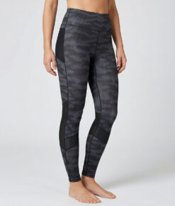 Kvinnlig modell visar ett par mörkgrå svarta mönstrade träningstights med hög midja. Modellen strår framifrån i en studio med ljusgrå bakgrund.
