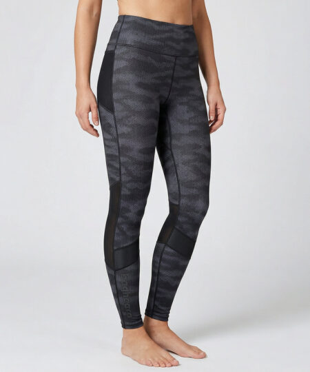 Kvinnlig modell visar ett par mörkgrå svarta mönstrade träningstights med hög midja. Modellen strår framifrån i en studio med ljusgrå bakgrund.