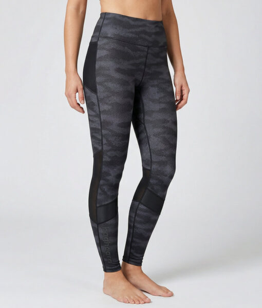 Kvinnlig modell visar ett par mörkgrå svarta mönstrade träningstights med hög midja. Modellen strår framifrån i en studio med ljusgrå bakgrund.