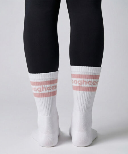 Kvinlig modell visar ett par Montana socks. Vita strumpor över svarta tights. Strumporna har rosa ränder och bagheera logo. Modellen står bakifrån i en studio med ljusgrå bakgrund.