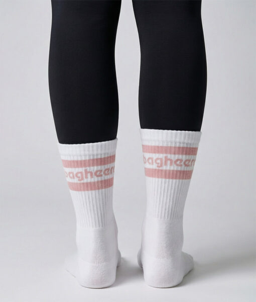 Kvinlig modell visar ett par Montana socks. Vita strumpor över svarta tights. Strumporna har rosa ränder och bagheera logo. Modellen står bakifrån i en studio med ljusgrå bakgrund.