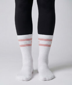 Kvinlig modell visar ett par Montana socks. Vita strumpor över svarta tights. Strumporna har rosa ränder och bagheera logo. Modellen står framifrån i en studio med ljusgrå bakgrund.