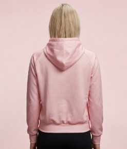 Kvinlig modell visar en rosa klassisk bagheera montana wct hoodie för dam. Modellen står bakifrån i en studio med ljusrosa bakgrund.