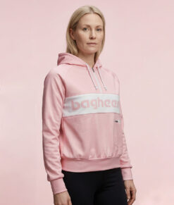 Kvinlig modell visar en rosa klassisk bagheera montana wct hoodie för dam. Modellen står snett framifrån i en studio med ljusrosa bakgrund.