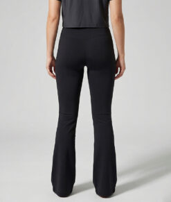 Kvinnlig modell visar ett par svarta mjuka och utsvängda tights. Modellen står bakifrån i en studio med ljusgrå bakgrund.