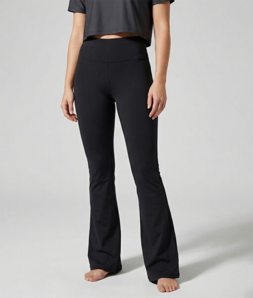 Kvinnlig modell visar ett par svarta mjuka och utsvängda tights. Modellen står framifrån i en studio med ljusgrå bakgrund.