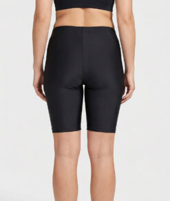 Kvinnlig modell visar ett par svarta korta tränings tights. Modellen står bakifrån i en studio med ljusgrå bakgrund.