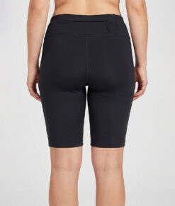 Kvinnlig modell visar ett par svarta slitstark korta trail tights. Modellen står bakifrån i en studio med ljusgrå bakgrund.