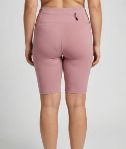 Kvinnlig modell visar ett par rosfärgade och svarta slitstark korta trail tights. Modellen står bakifrån i en studio med ljusgrå bakgrund.