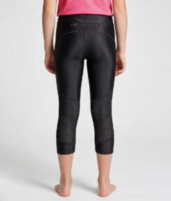 En tjejmodell på 12 år visar ett par svarta 3/4 långa race tights. Modellen står bakifrån i en studio med ljusgrå bakgrund.