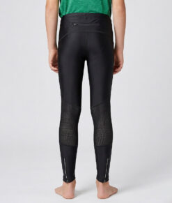 En killmodell i 12 års åldern visar ett par svarta långa tights. Modellen står bakifrån i en studio med ljusgrå bakgrund.