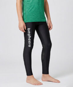 En killmodell i 12 års åldern visar ett par svarta långa tights. Modellen står framifrån i en studio med ljusgrå bakgrund.