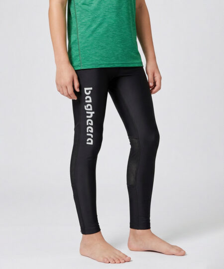 En killmodell i 12 års åldern visar ett par svarta långa tights. Modellen står framifrån i en studio med ljusgrå bakgrund.