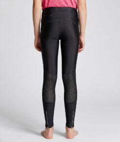 En tjejmodell i 12 års åldern visar ett par svarta långa tights. Modellen står bakifrån i en studio med ljusgrå bakgrund.