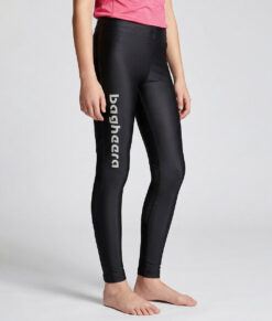 En tjejmodell i 12 års åldern visar ett par svarta långa tights. Modellen står framifrån i en studio med ljusgrå bakgrund.