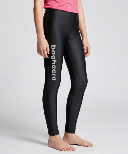 En tjejmodell i 12 års åldern visar ett par svarta långa tights. Modellen står framifrån i en studio med ljusgrå bakgrund.