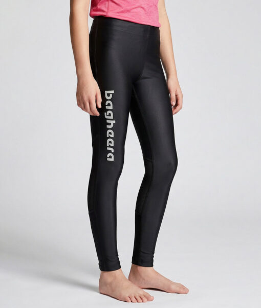 En tjejmodell i 12 års åldern visar ett par svarta långa tights. Modellen står framifrån i en studio med ljusgrå bakgrund.