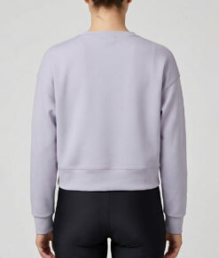 Kvinlig modell visar vår lavendelfärgade magkorta Cloud Crop Sweater bakifrån mot en ljusgrå bakgrund.